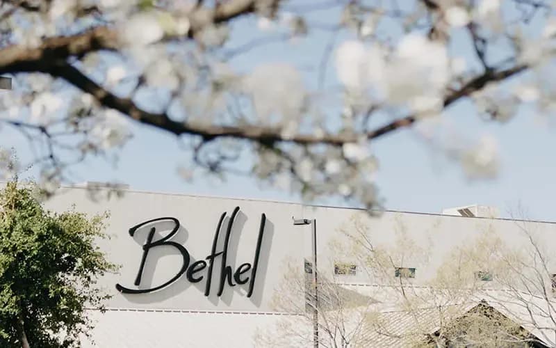 Exterior of Bethel Church building with the Bethel sign visible above the entrance, framed by blossoming trees
