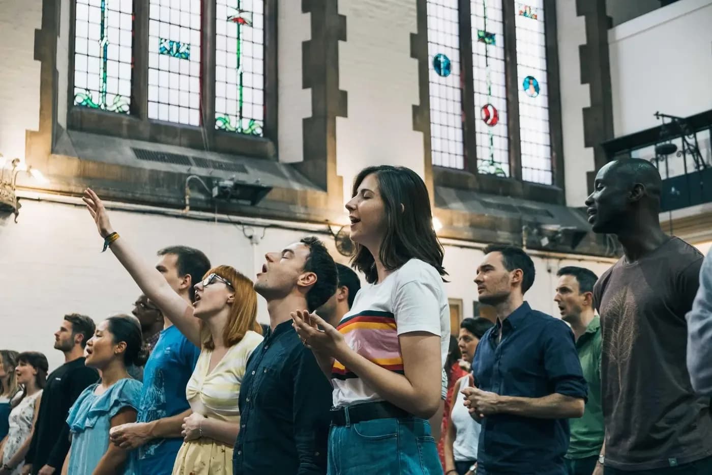 Congregation singing during a worship service inside the church, with stained glass windows in the background
