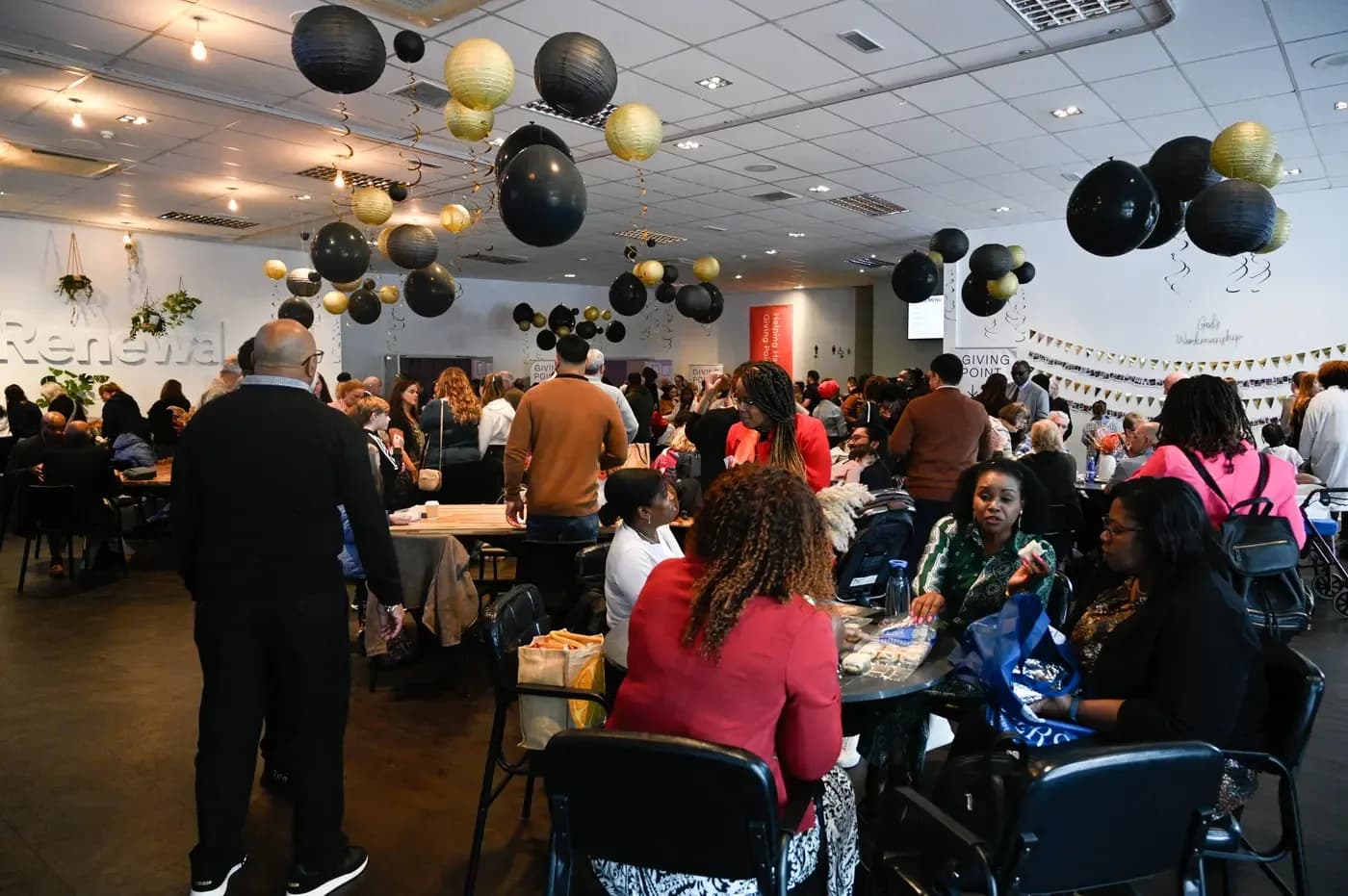 Interior of Renewal Church hall with congregation gathered at tables, 'Renewal' signage on the wall