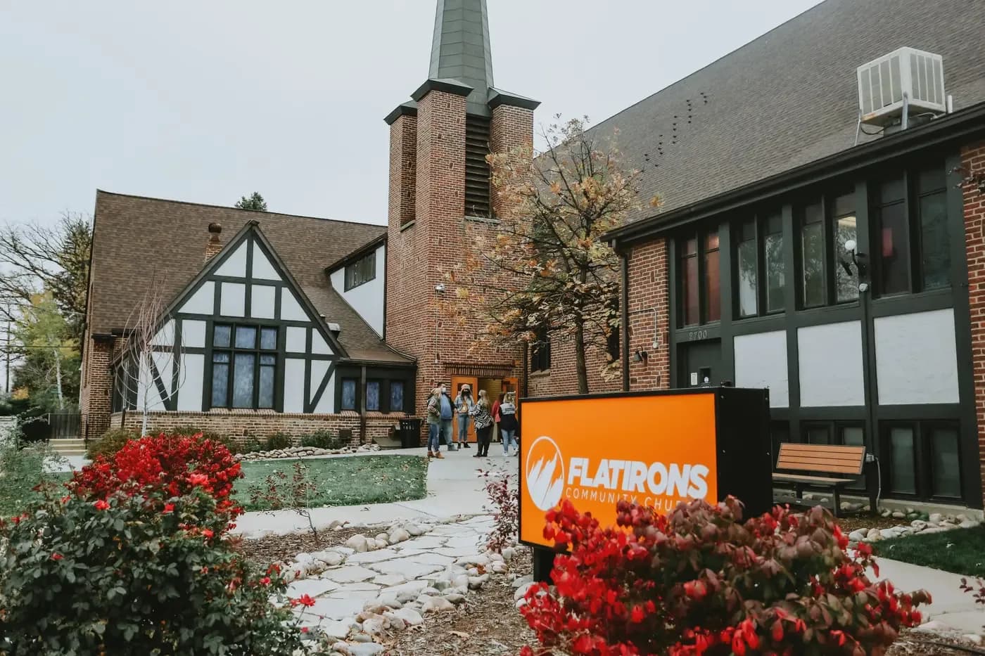 Exterior of Flatirons Community Church with brick building, steeple, and orange Flatirons sign