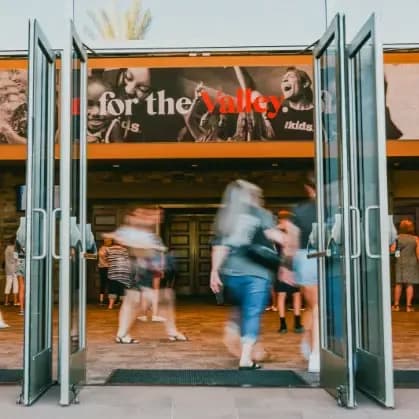 Church entrance with people walking through open glass doors beneath a 'for the Valley' banner